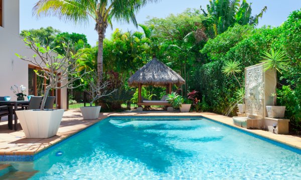 A beautiful backyard design featuring a pool and a tiki hut.