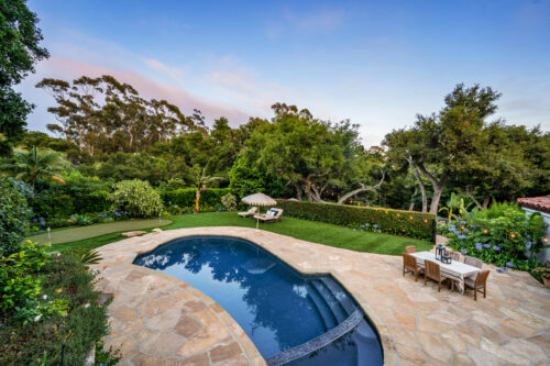 A backyard pool landscaping idea featuring a swimming pool, lush greenery, and outdoor furniture
